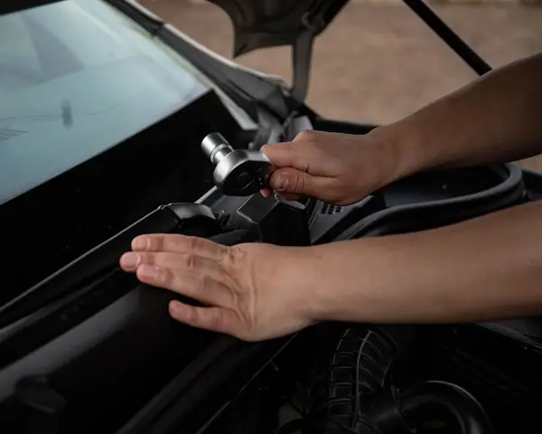Hands fitting a part under the base of a windshield on an open engine bay